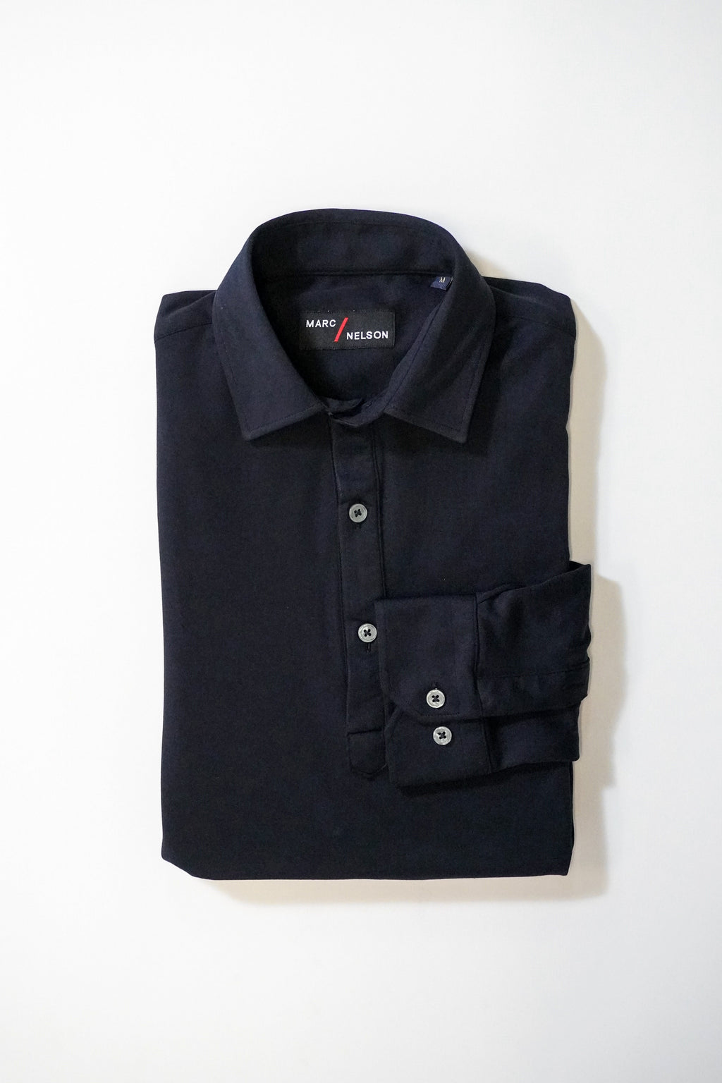 A neatly folded long-sleeve black collared shirt with buttons, displayed on a plain white background. The label inside the collar reads Maro Nelson.