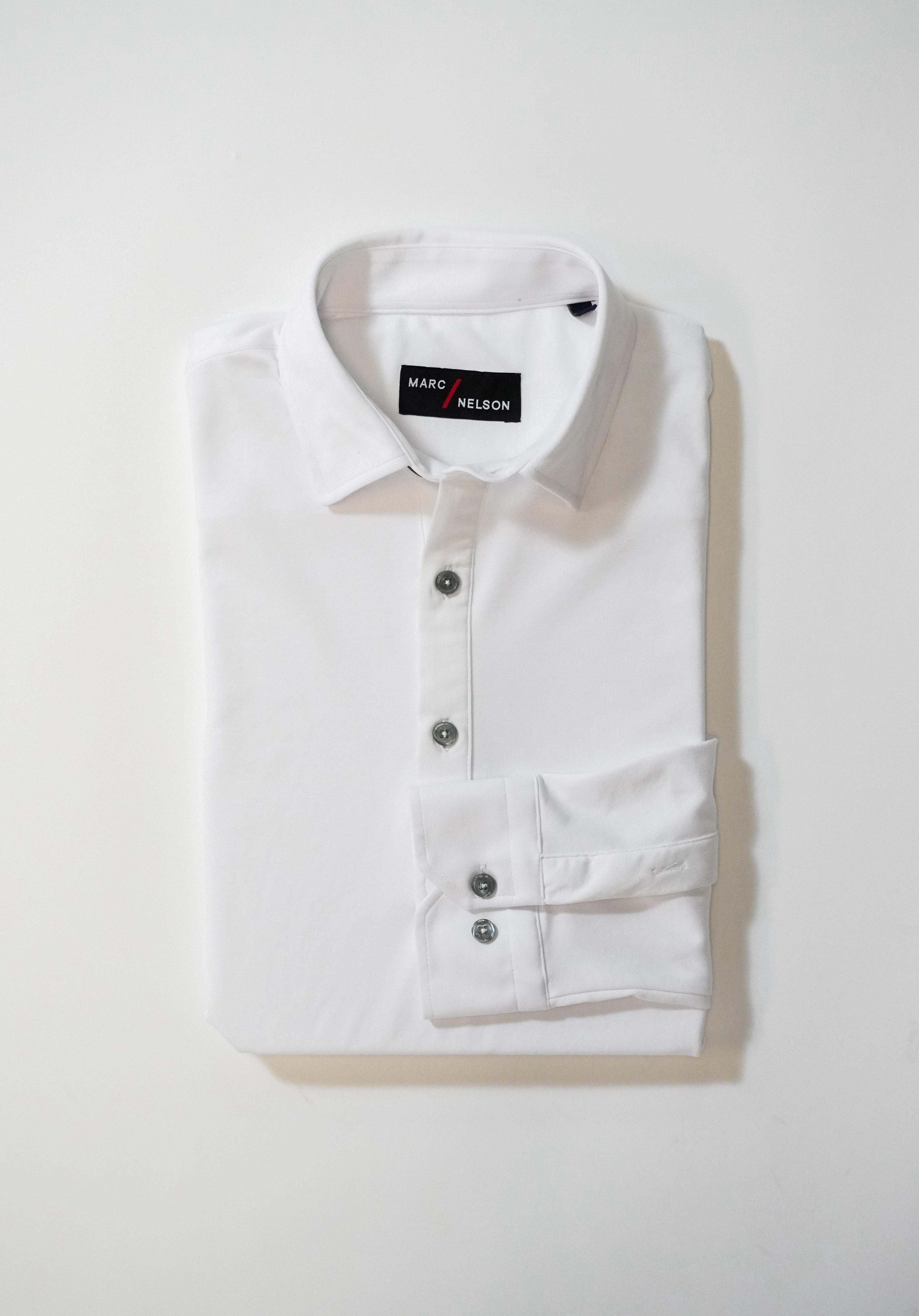 A neatly folded white button-up shirt with a collar and three visible buttons, placed on a white surface. The label inside the collar reads MARC NELSON.